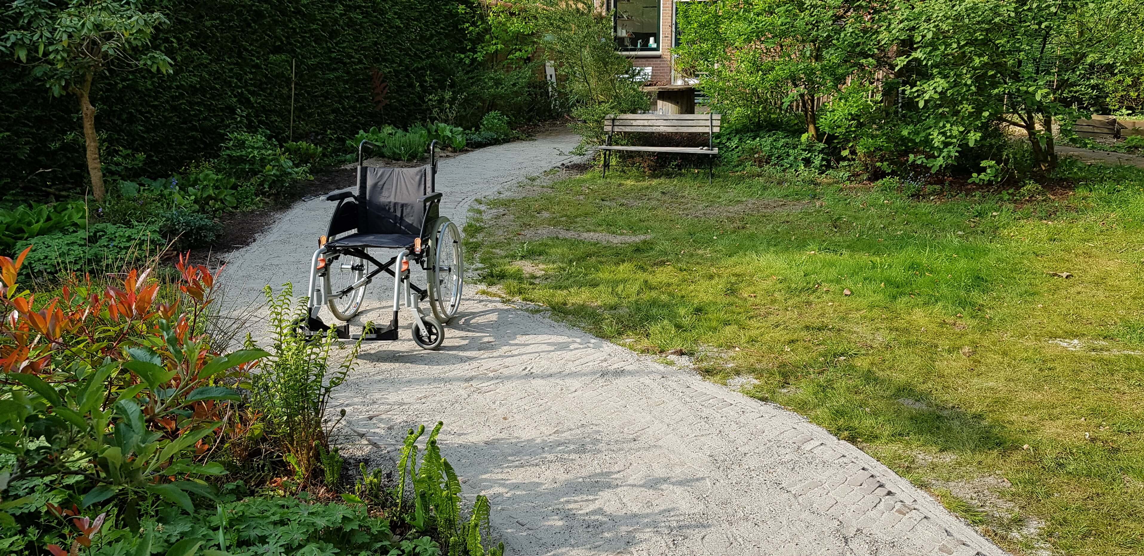 Opvouwbare rolstoel op rolstoeltoegankelijk tuinpad van waalformaat klinkers dat door collegae is aangelegd