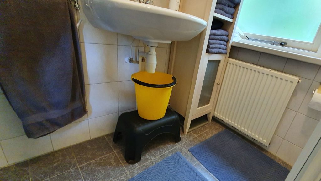 Emmer op krukje onder wasbak om water te besparen bij het doorspoelen van de wc