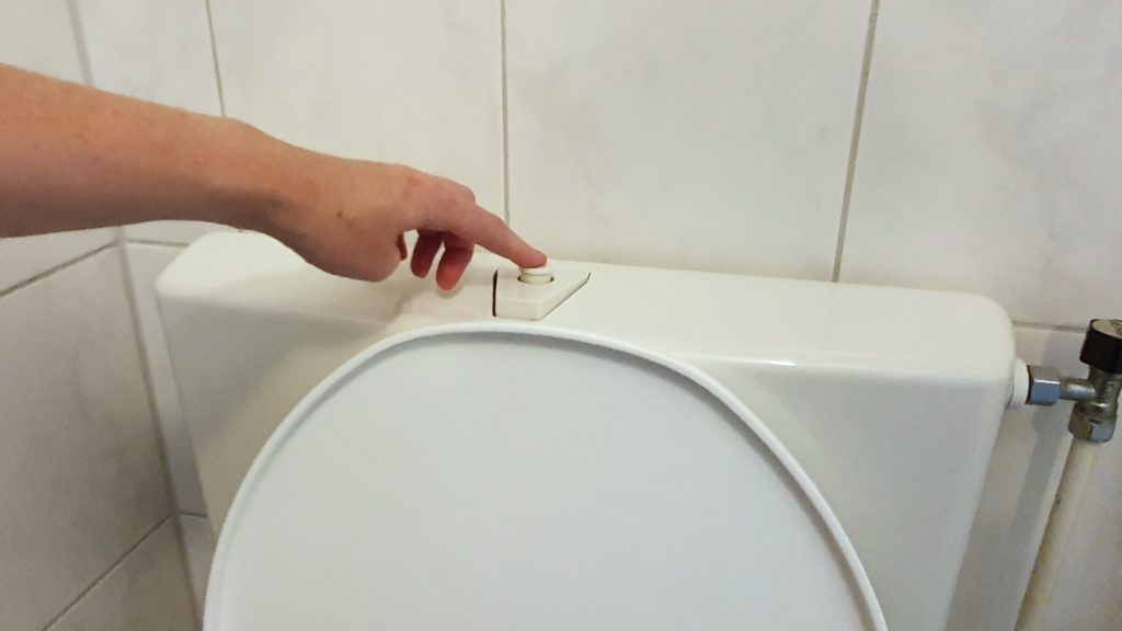 Vinger bij de stopknop van de stortbak om zoveel mogelijk water te besparen bij het doortrekken van de wc