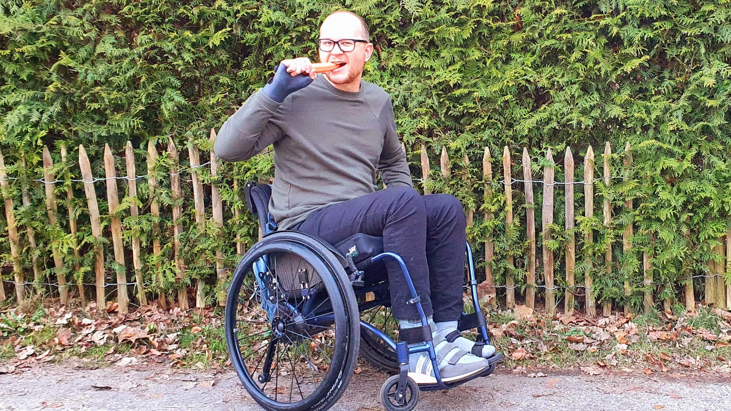 Foto van een man in een maatwerk rolstoel die een wortel eet ter illustratie van hoe raar het voorstellen van een worteldieet is aan een brilgebruiker