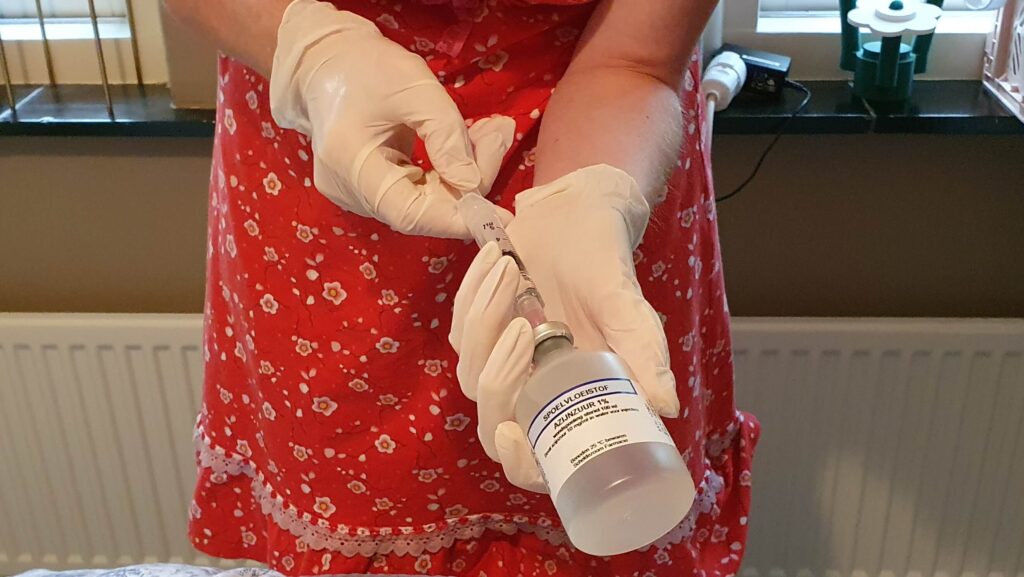 foto van een verpleegster in een rood jurkje die spoelvloeistof in een injectiespuit doet, waardoor ze een beetje op Florence Nightingale lijkt