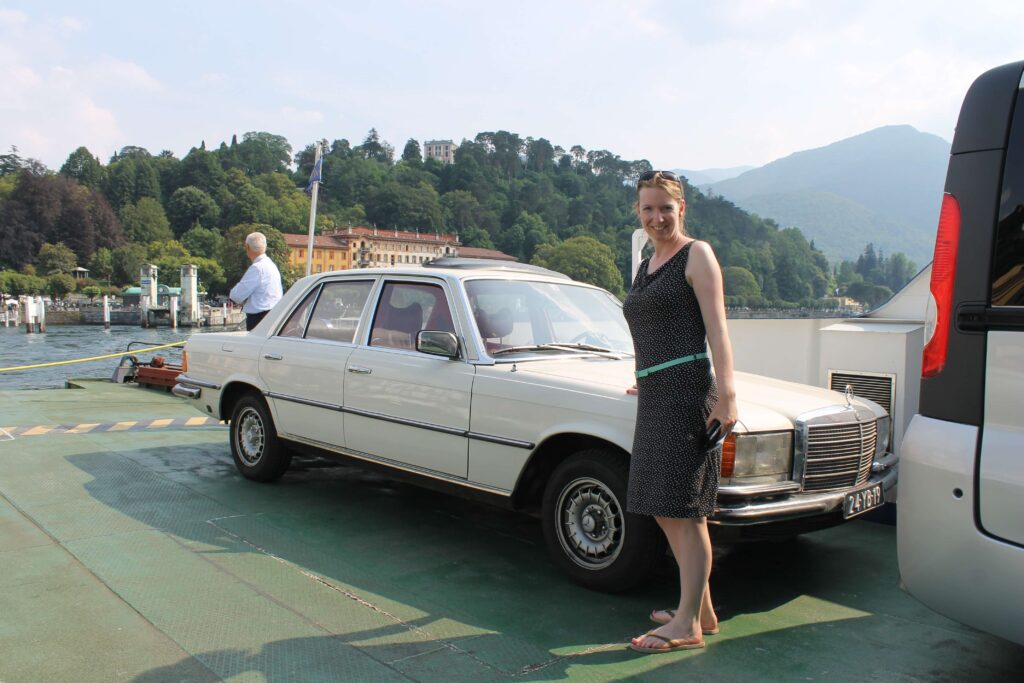 Mercedes-Benz W116 op de pont van het Como Meer tussen Menaggio en Bellagio Italië met daarbij de trotse eigenaresse