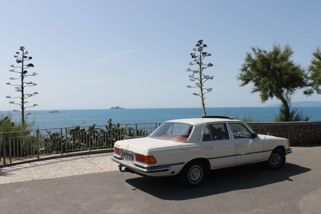 Foto van een witte Mercedes-Benz W116 met rood interieur geparkeerd langs het comomeer oftewel lago di como.