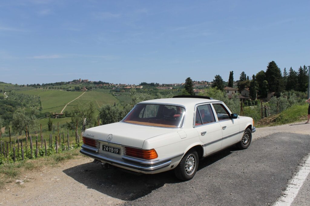 foto van een klassieke oldtimer van Mercedes-Benz W116 in de heuvels van Toscane met op de achtergrond wijngaarden