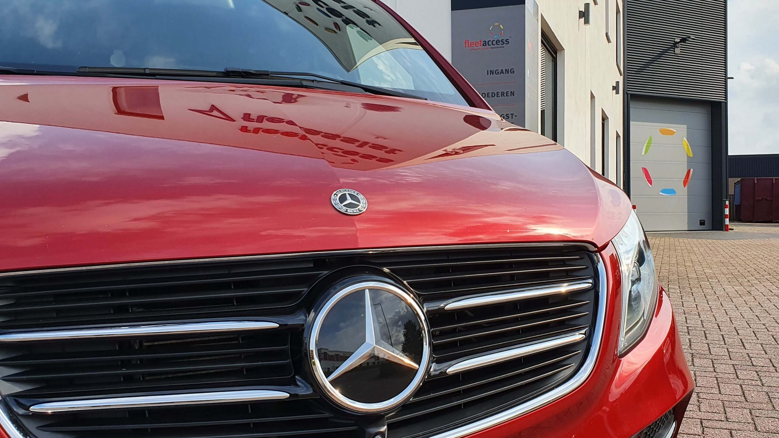 Voorkant van een rode Mercedes-Benz V-Klasse met op de achtergrond het pand met logo van Fleetaccess alarmsystemen