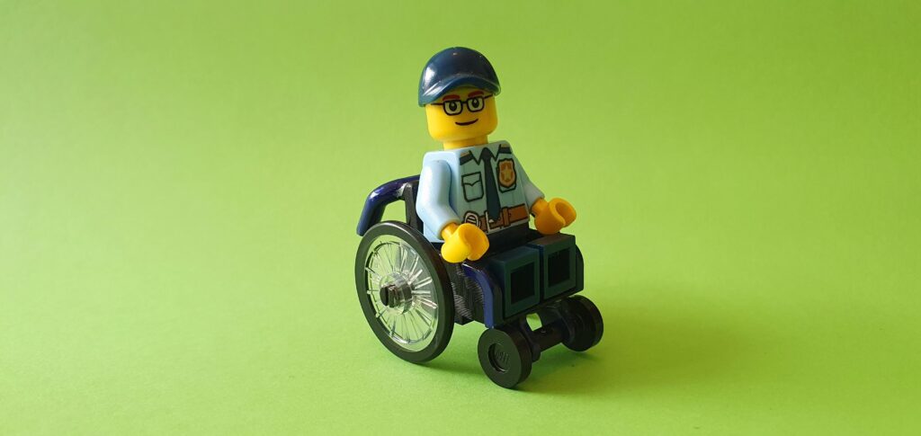 LEGO SigFig van RaGaSto waarbij het LEGO poppetje een politie uniform draagt, een dark blue baseball cap draagt en zit in een geverfde LEGO rolstoel MOC.