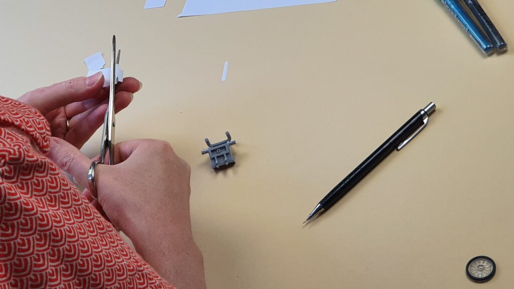 afbeelding van het knippen van een papieren mal tbv de carbonlook plakfolie die op het rolstoeltje in het midden van de foto geplakt kan worden tbv een LEGO SigFig van RaGaSto