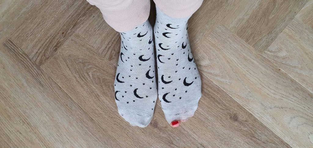 Foto van twee voetjes in vrolijke sokken waarvan een grote teen met nagellak door een gat in de sok uitsteekt