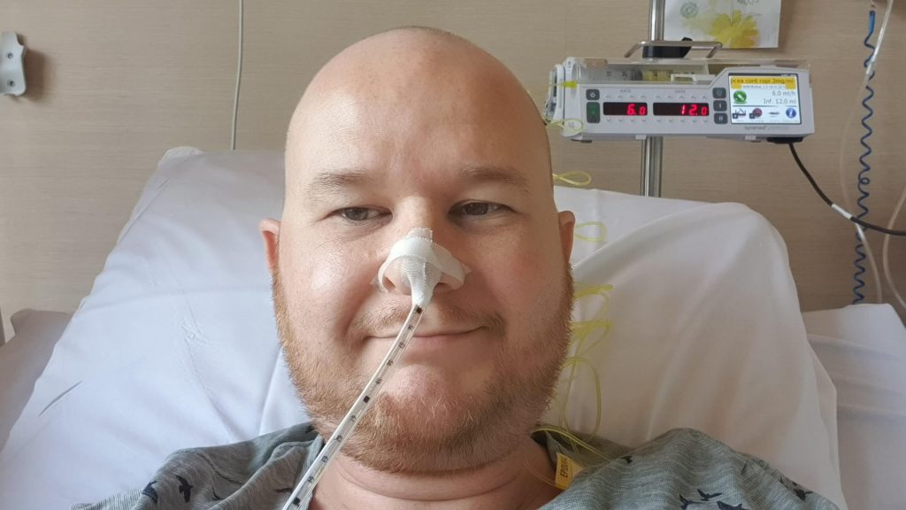 Foto van een kale man met baard die in een ziekenhuisbed ligt en een maaghevel of neussonde heeft in zijn neus na de aanleg van een stoma, behorend tot de blogs van RaGaStoma