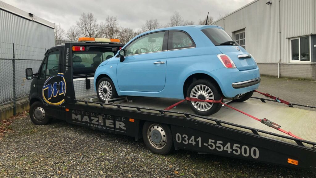 Foto van een lichtblauwe Nuova Fiat 500 die na het aankopen en importeren op de autoambulance van Autobedrijf Mazier naar Ermelo werd gebracht voor ons als klant.