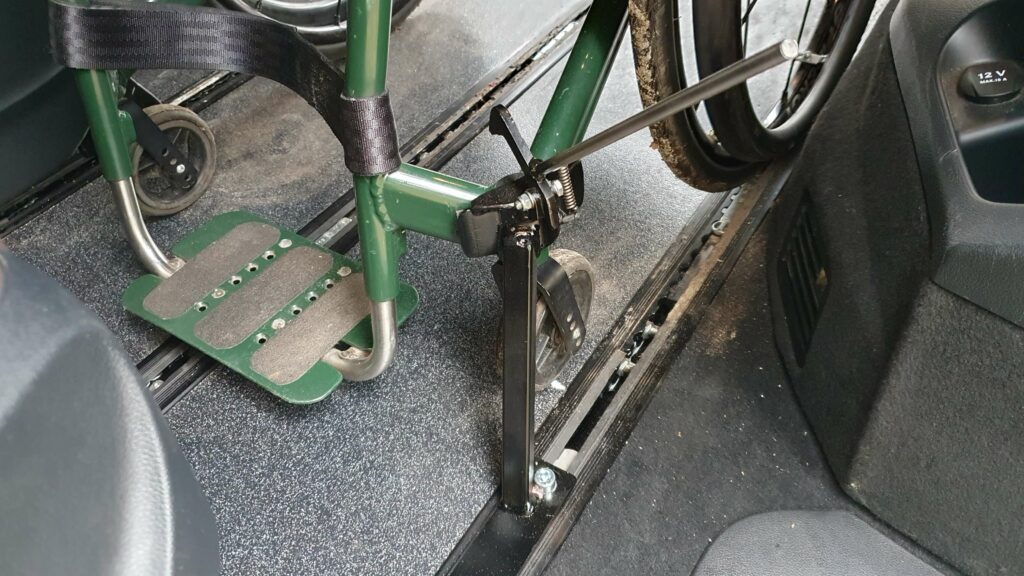 Foto van een op maat gemaakte en gelaste klem om een rolstoel vast te zetten in een rolstoelbus, zodat de rolstoel niet door de bus vliegt in noodsituaties. De rolstoelklem zit vast in de standaard vloerrails van een Mercedes-Benz V-Klasse.