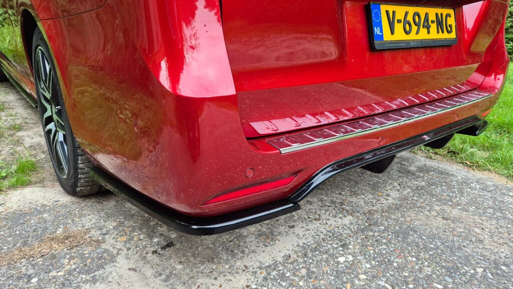 Close-up van de Maxton Design diffusor met achter splitters gemonteerd op de achterbumper van een rode Mercedes-Benz V-Klasse AMG-Line. De bodykit van Maxton is glanzend zwart uitgevoerd.