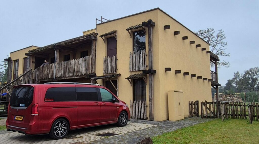 foto van het mooiste rolstoelbusje van nederland, oftewel een rode mercedes-benz V-Klasse, geparkeerd op de eigen gehandicaptenparkeerplaats voor de deur van de rolstoeltoegankelijke kamer van Safari Resort Beekse Bergen. Het appartement met de hotelkamers is in typisch Afrikaanse sferen gebouwd.