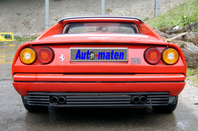 De achterkant van een Ferrari 328 GTS in de kleur Rosso Corsa. De kentekenplaat is onherkenbaar gemaakt door het logo van de verdwenen website Auto-Maten.nl. Die websitenaam is ook te lezen in het logo.