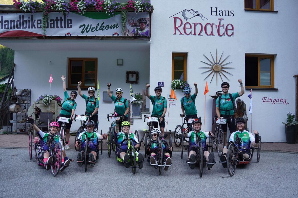 Teamfoto van Birds on Wheels tijdens de HBB-week van 2026. Het team staat opgesteld voor pension Haus Renate in het Kaunertal. De handbikers staan op de voorgrond opgesteld met daarachter ieder zijn of haar eigen buddy en hun racefietsen. De handbikers zitten in hun handbike en dragen het wedstrijdshirt en de buddy's dragen het teamshirt van Birds on Wheels van revalidatiecentrum Vogellanden. H3.1 handbiker Ralph Stoové staat helemaal rechts op de foto met zijn buddy Jonas.