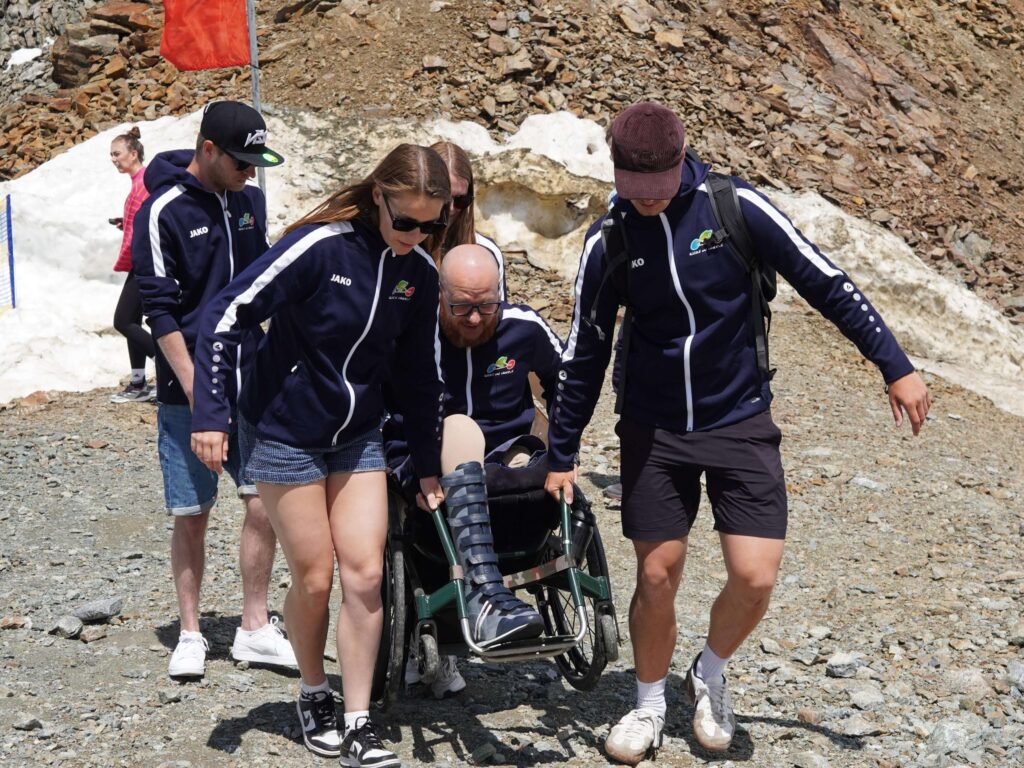 Ralph Stoové wordt in zijn rolstoel door een aantal buddy's van team Birds on Wheels Vogellanden getild en over puin en rotsen naar de bergtop van de Kaunertaler Gletsjer gedragen. Het team draagt blauwe teamkleding met het logo van het team. Ralph heeft een groene rolstoel van TNS en draagt net als de anderen een korte broek. Ralph heeft links een hoge bovenbeenamputatie en rechts draagt hij een hoge orthopedische laars met enkelvoetorthese om zijn verlamde been.